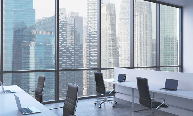 Workplaces in a bright modern open space office. White tables equipped with modern laptops and black chairs. Singapore panoramic view in the windows. 3D rendering.